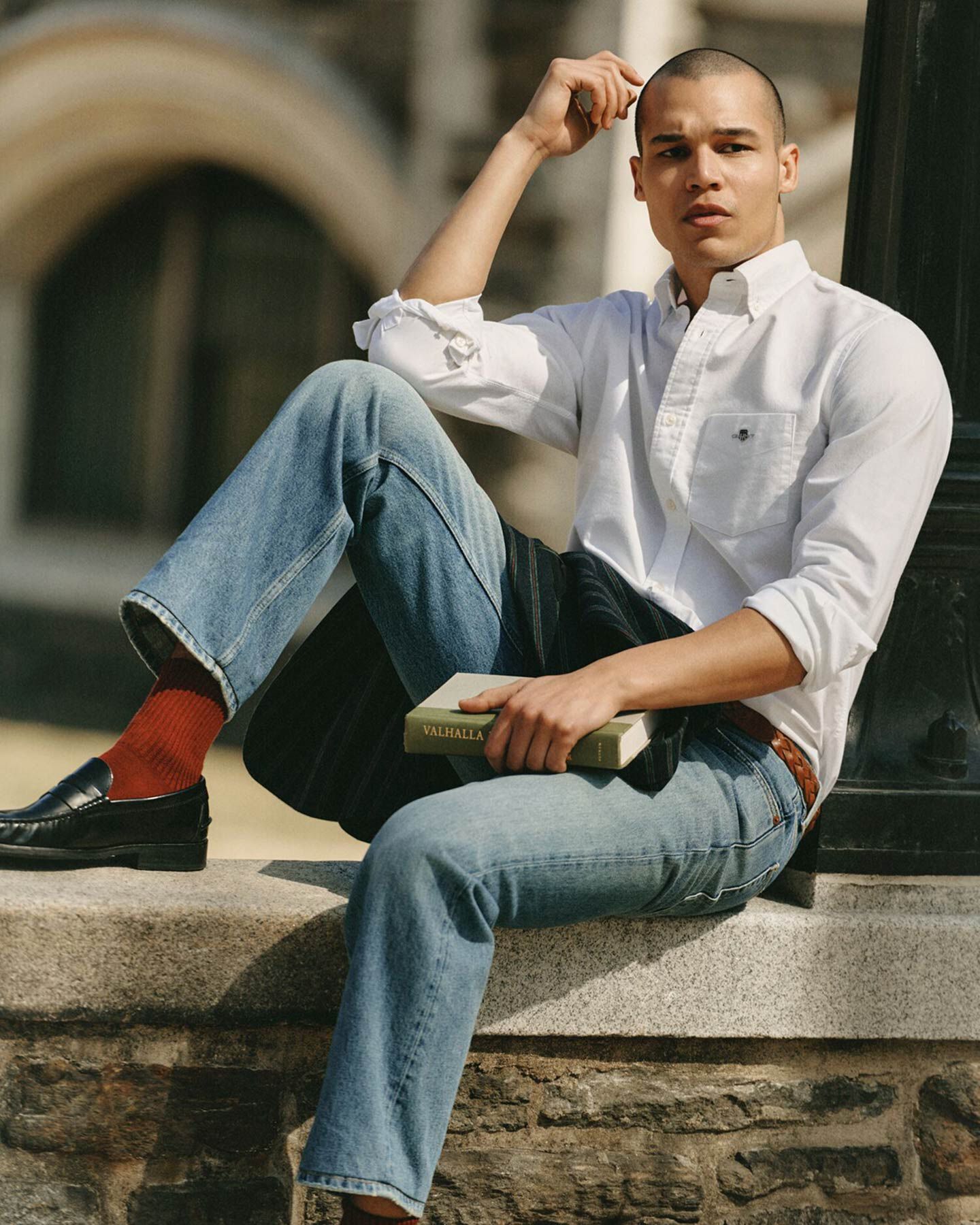 Men wearing Gant white shirt and blue jeans sits on stone ledge